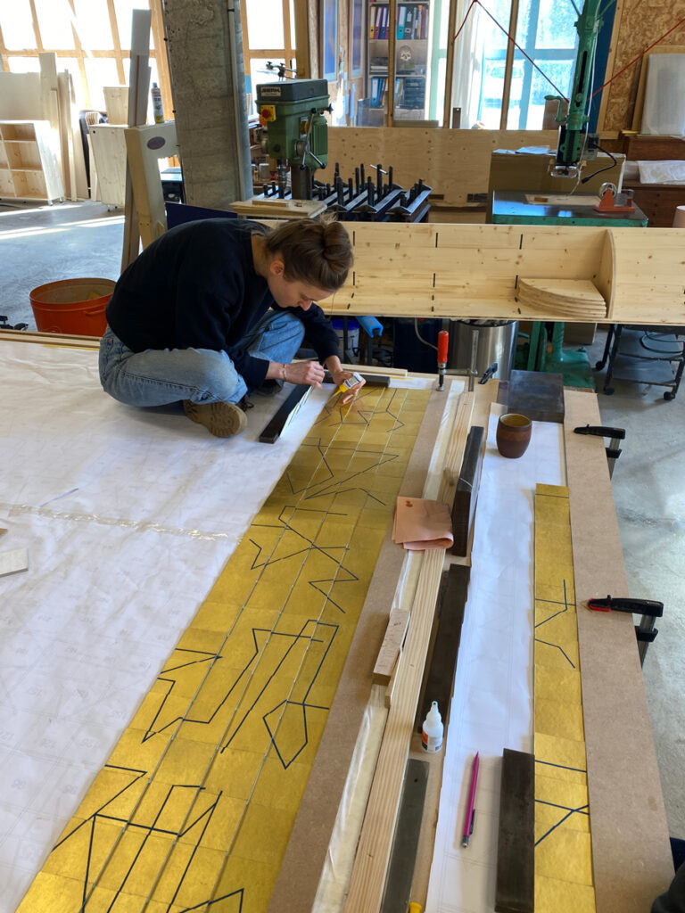 Victoire Camus dans l'atelier de marqueterie de Pierre-Henri Beyssac, pendant le montage de leur cocréation "Memento", marqueterie de papier suspendue, dorée à la feuille d'or